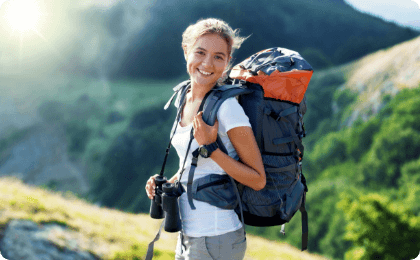 A woman with a hiking bag happily smiling while holding a pair of binoculars