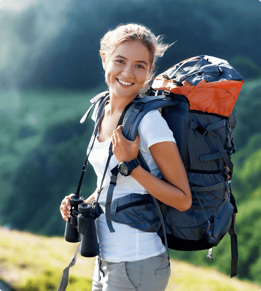 A woman with a hiking bag happily smiling while holding a pair of binoculars