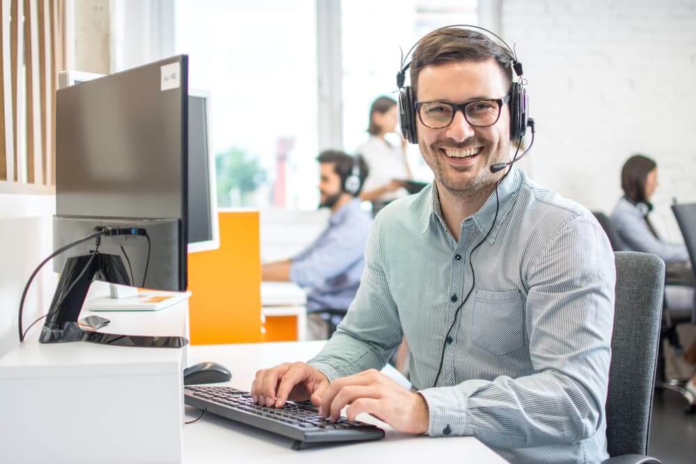 Smiling customer service representative wearing a headset and working at a computer.