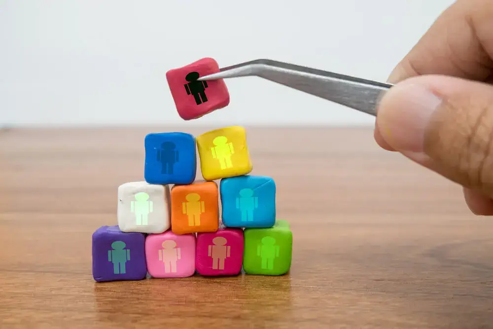A hand using tweezers to pick up a colorful block with a human icon