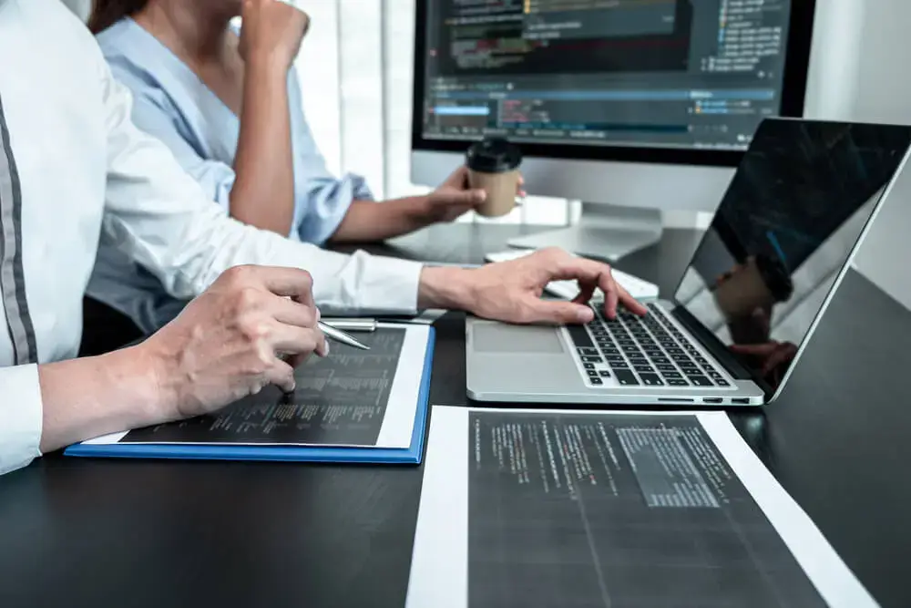 Two professionals collaborating on a project, reviewing documents and working on a laptop