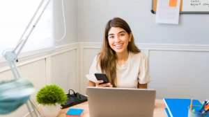 a happy business owner on the computer and their phone speaking to their remote social media virtual assistant