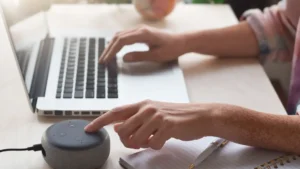 What Can an Amazon Virtual Assistant Do for Your Business - Person using a laptop and interacting with a smart speaker on a desk.
