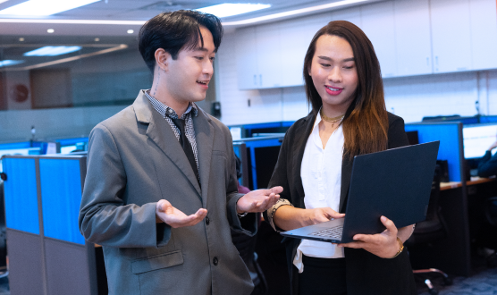 Two individuals with one holding a laptop and the other one explaining