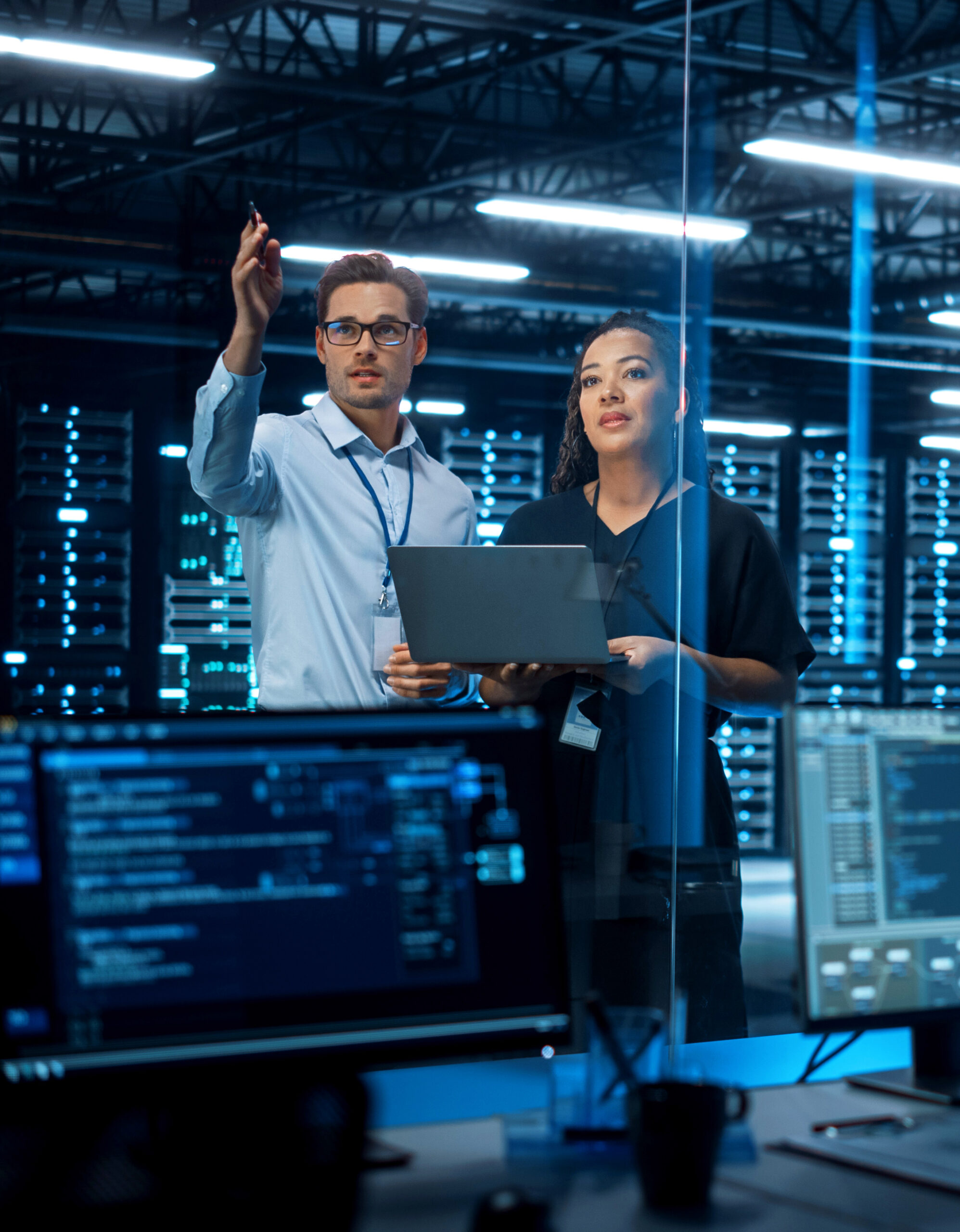 Two IT professionals discussing in a server room with monitors and equipment.