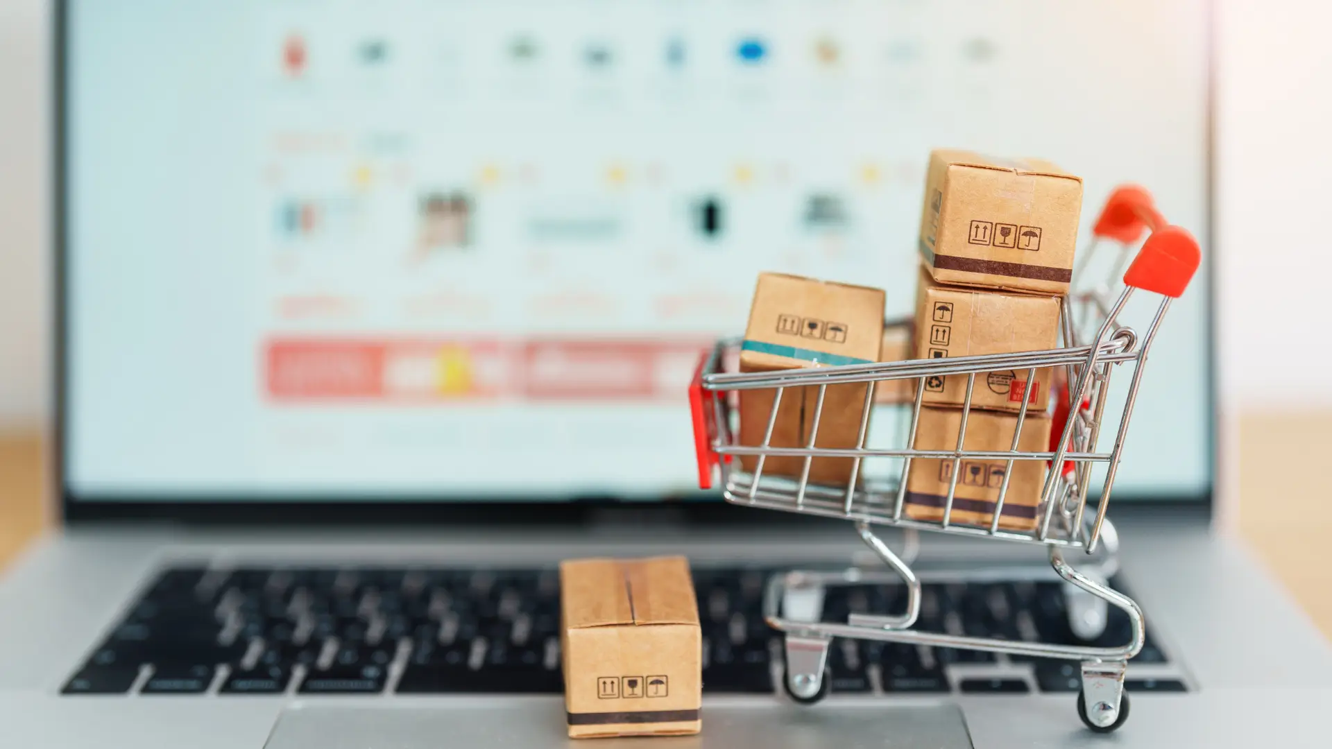 Mini shopping cart with small packages on a laptop keyboard, symbolizing online shopping.