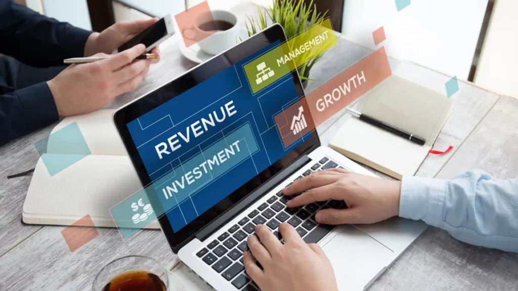 Person using a laptop with floating business-related terms like "REVENUE," "INVESTMENT," and "GROWTH."