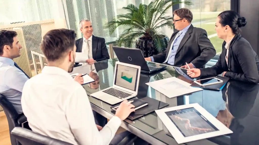 A group of business professionals discussing documents and data during a meeting in a modern office setting