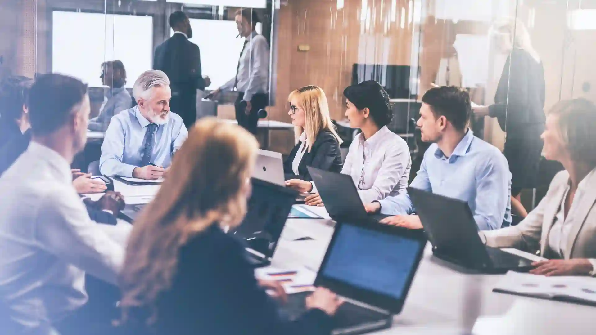 A group of professionals in a meeting, working on laptops around a conference table.