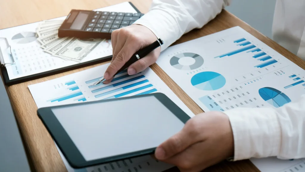 Person analyzing financial charts with a tablet and calculator on the desk.