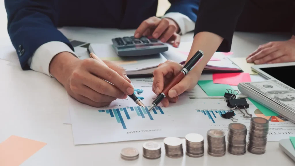 Business people reviewing financial charts with calculator and stacked coins on desk