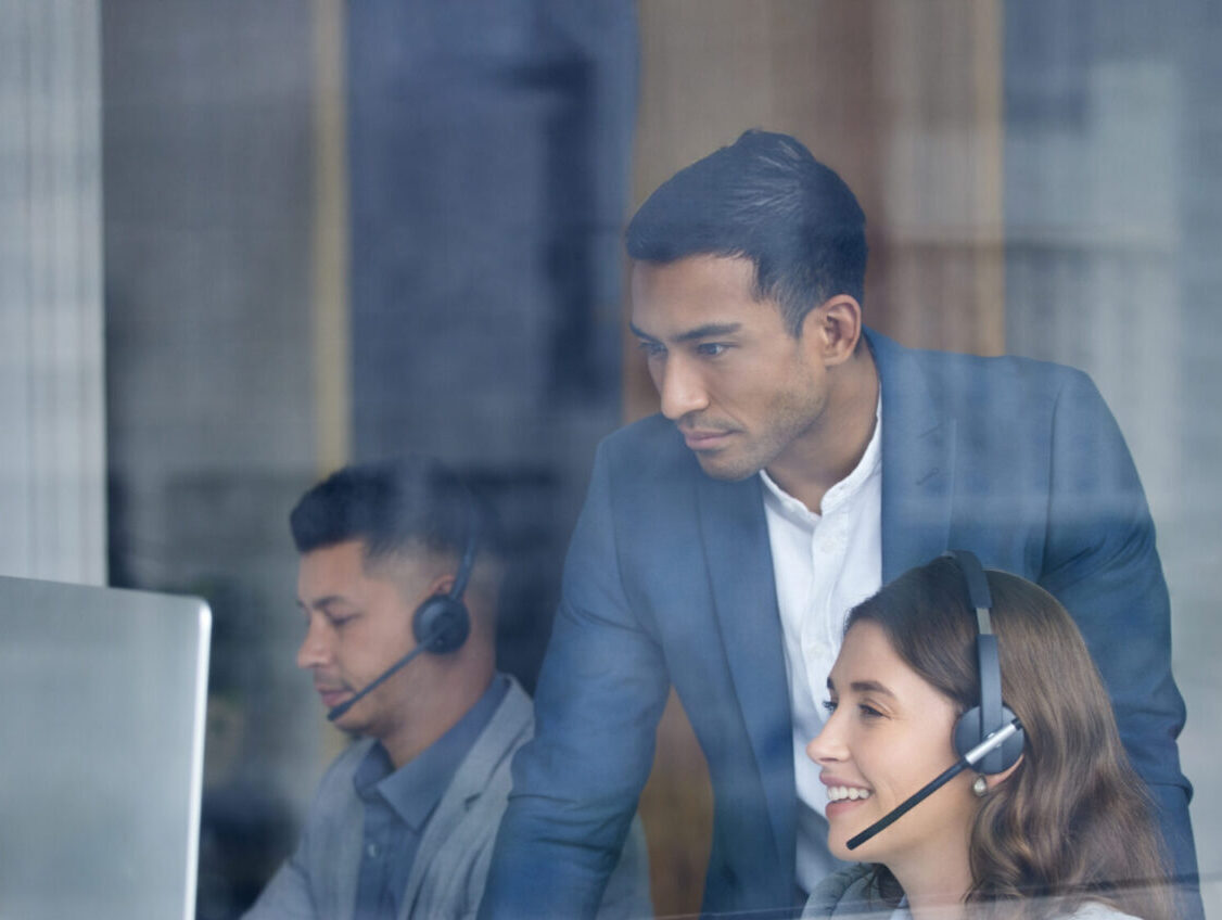 Team of customer support representatives wearing headsets working at computers.