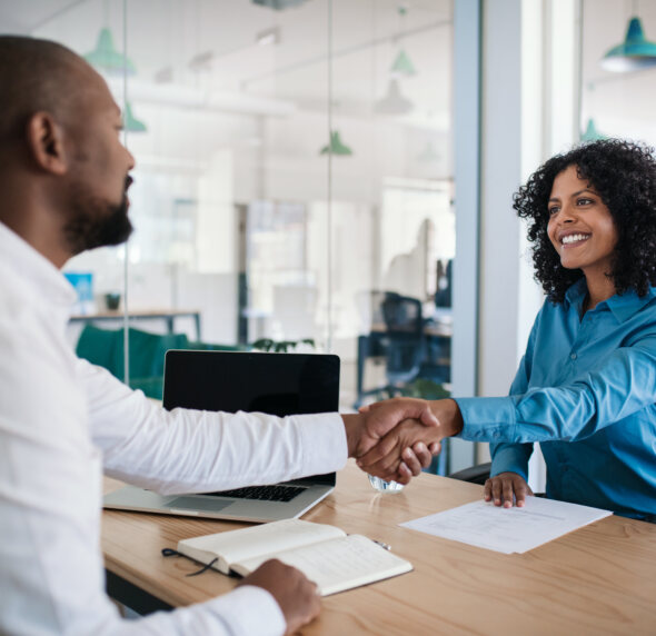 Insurance agent shaking hands with a client across a desk after signing a policy agreement