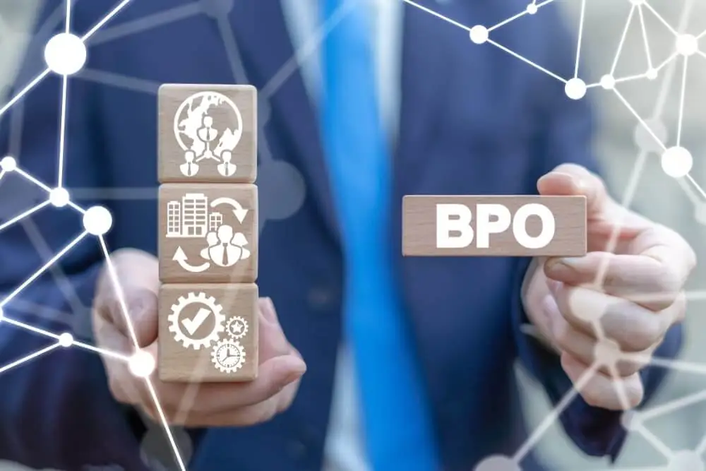 A person in a suit holding wooden blocks with icons representing business processes and a block labeled 'BPO